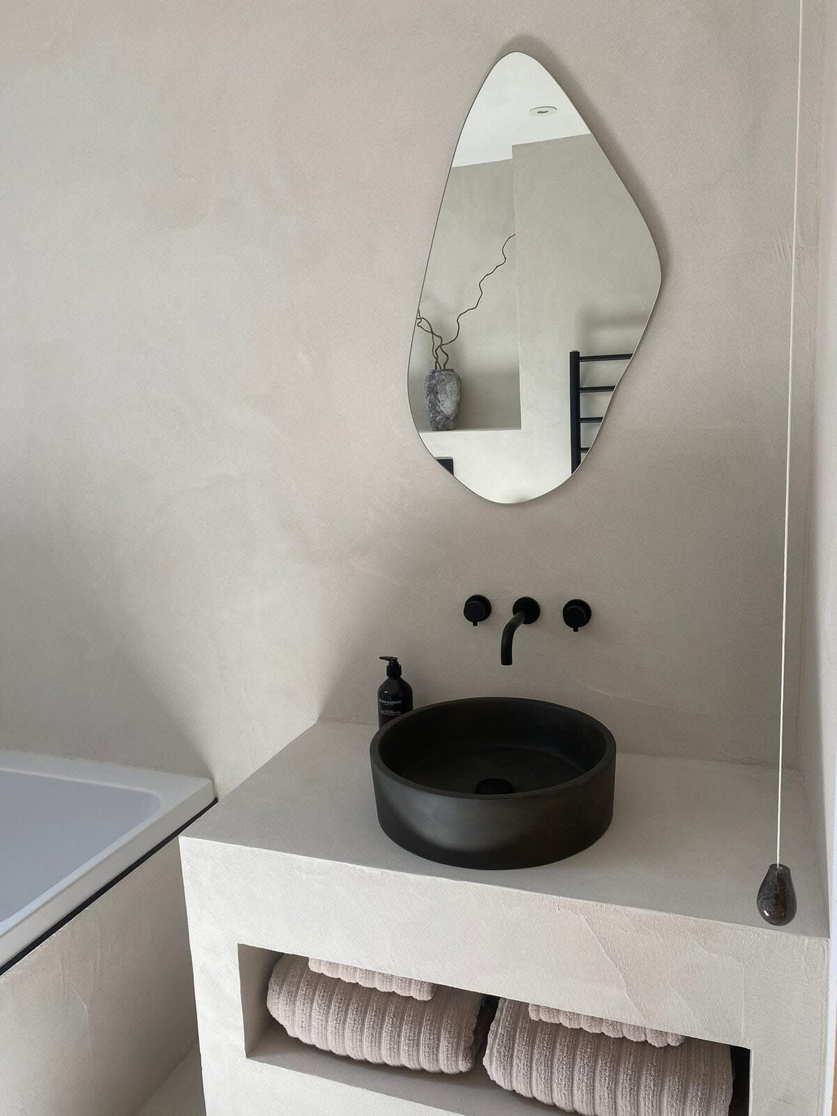 Cream microcement bathroom with black basin and wall-mounted taps